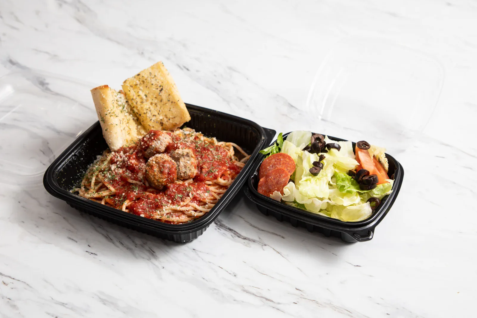 An individually packed Brooklyn Pizzeria pasta meal with salad and garlic bread