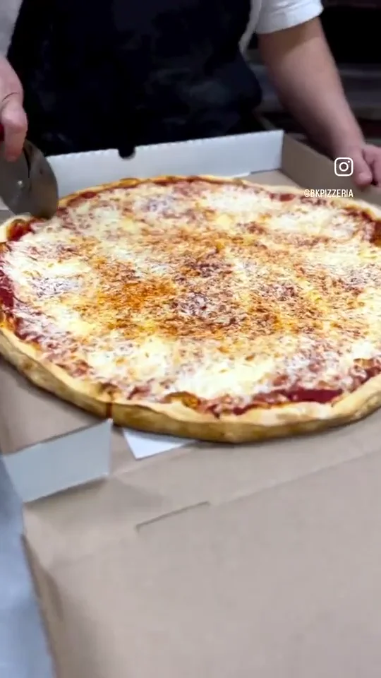 A Brooklyn Pizzeria team member cutting a freshly baked cheese pizza